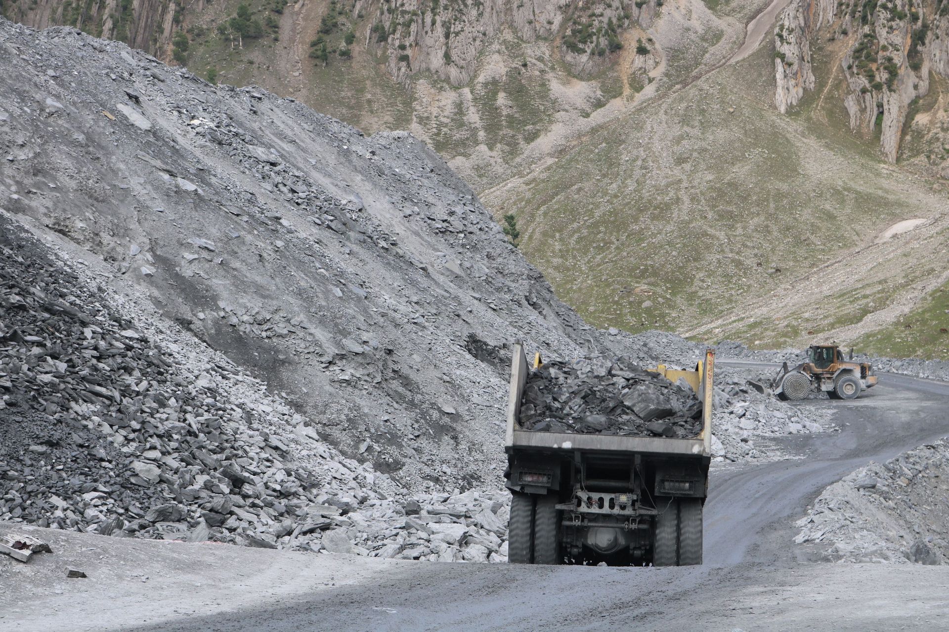 A quarry with trucks and machinery operating amidst rugged mountain terrain.