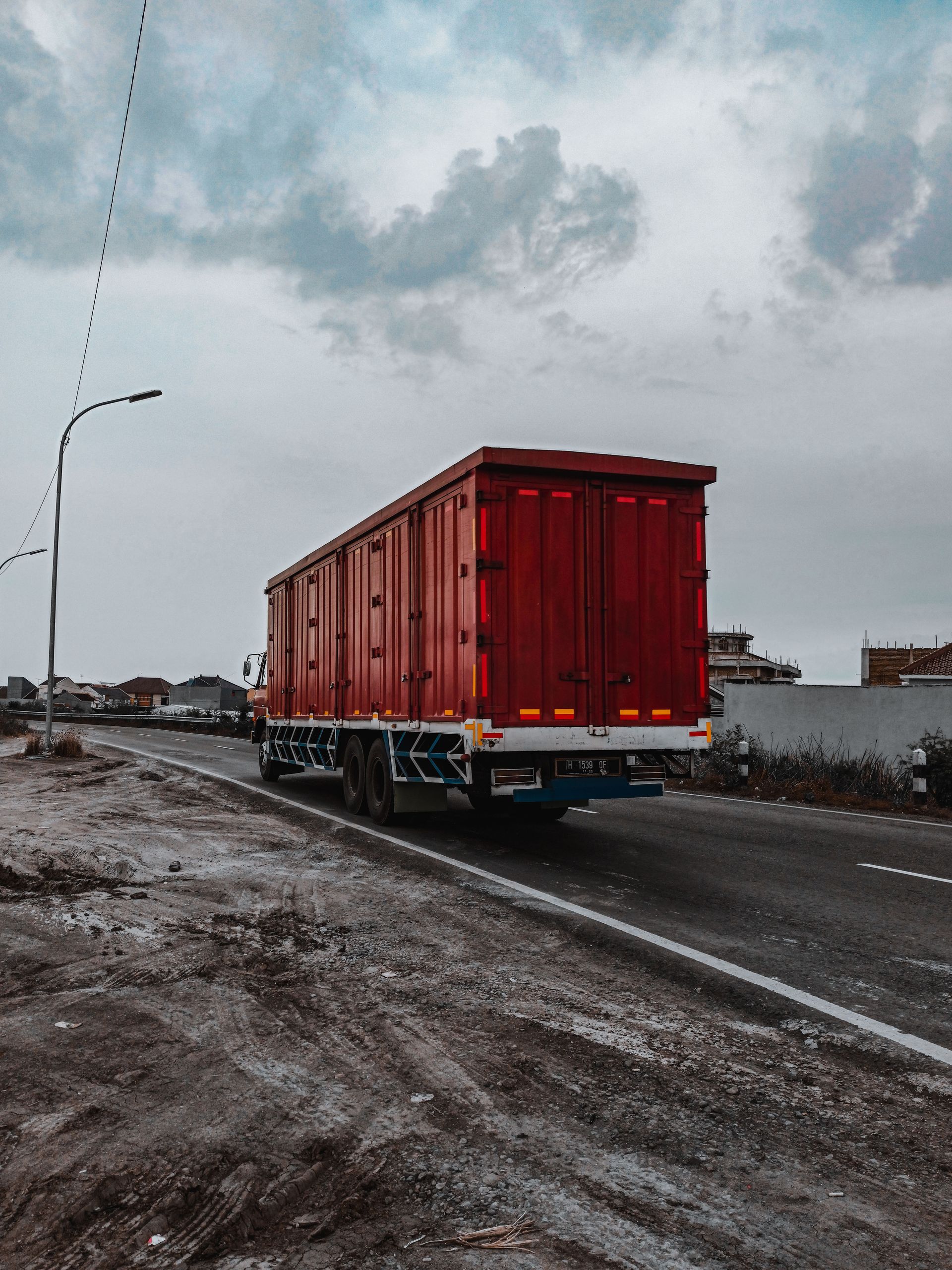 Large heavy motor vehicle driving on roadway while transporting goods along village in cloudy day